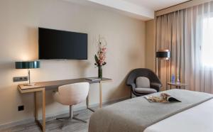 a hotel room with a bed and a desk and a tv at NH Collection Madrid Suecia in Madrid