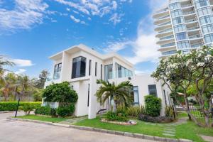 a white house with palm trees and a tall building at ARIA Resort Vung Tau S01 in Vung Tau
