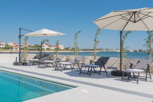 a pool with tables and chairs and umbrellas at Seafront Villa Serena with pool and seaview in Privlaka