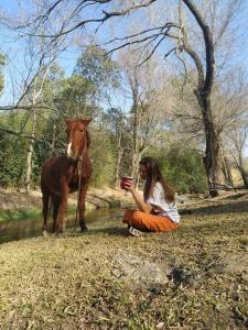 una mujer sentada en el suelo junto a un caballo en Chalet del arroyo, en La Porteña