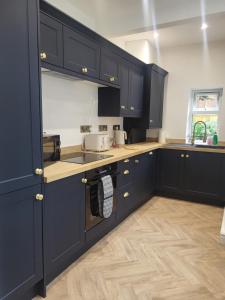 a kitchen with navy blue cabinets and wooden floors at Relaxing Seaside Stay 3-Bed Home Minutes from Hythe Beach in Hythe