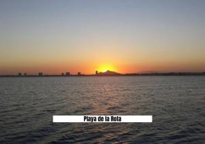 a sunset over the water with a sign that says play me lie me hug at Apartalux San Pedro Mar in San Pedro del Pinatar