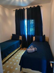 two beds in a room with blue curtains at lagoon apartment 4 in Moulay Bousselham