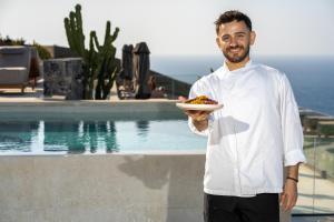 a man holding a plate of food next to a pool at Happy Cretan Suites in Agia Pelagia