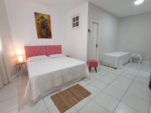 a white bedroom with a large bed with a pink headboard at Pousada das Flores in Conservatória