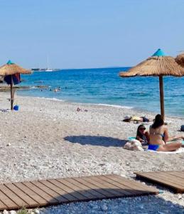 two people sitting on the beach under an umbrella at Spacious 2BR by Floisvos Beach Saltwater Balcony in Athens