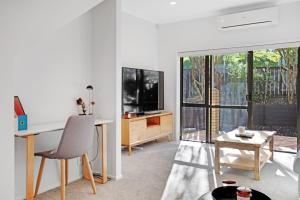 a white living room with a desk and a tv at Sweet Sunshine Nest with Pool, Aircon and Parking in Auckland