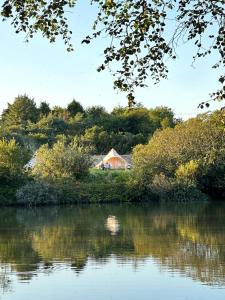 a house on a hill next to a body of water at Mallard - 5m Luxury Bell Tent at Tregonetha Lake - Tylda Tents in Saint Columb Major