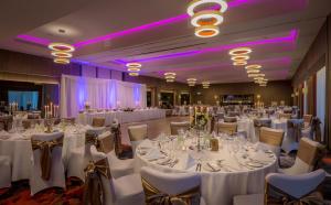 un salón de banquetes con mesas y sillas blancas e iluminación púrpura en Clayton Hotel Chiswick en Londres