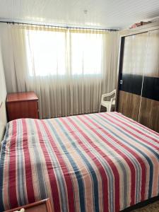 a bedroom with a bed with a striped comforter and a window at Quartinho da Tranquilidade in Divinópolis