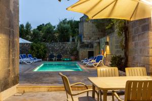 a swimming pool with chairs and a table and an umbrella at Tal-Masklu farmhouse in Għarb
