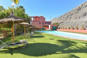 a resort with a swimming pool with chairs and an umbrella at Puerto Marina 10 - Pasito Blanco in San Bartolomé de Tirajana