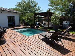 eine Holzterrasse mit einem Pool, einem Tisch und Stühlen in der Unterkunft Villa moderne avec piscine chauffée in Artigues-près-Bordeaux