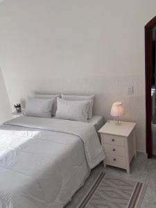 a white bedroom with a large bed and a night stand at Casa Refúgio Canto da Viola in São Roque