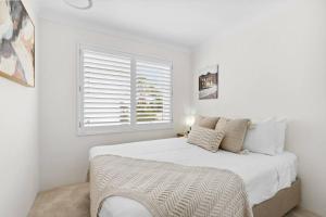 a white bedroom with a large bed and a window at Beachfront Bliss Where Sea Breeze Meets Style in Narrabeen