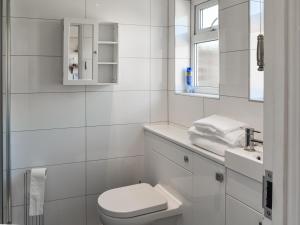 a white bathroom with a toilet and a sink at Selkie Cottage in Corton +2 photos
