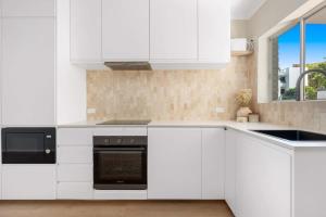 una cocina con armarios blancos y horno negro en Direct Ocean Front Apartment, en Redcliffe
