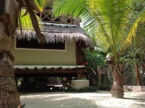 een huis met een rieten dak en een palmboom bij La Casa de Juan in Holbox Island