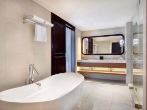 a bathroom with a tub and a sink and a mirror at Grand Mercure Bali Seminyak in Seminyak