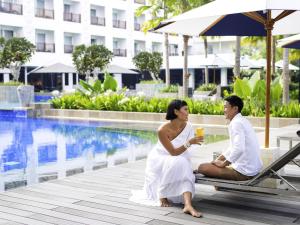 a man and a woman sitting on a lounge chair by a pool at Grand Mercure Bali Seminyak in Seminyak