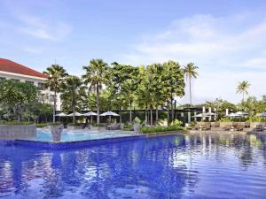 a pool at a resort with palm trees and umbrellas at Grand Mercure Bali Seminyak in Seminyak