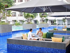 a man and woman sitting on a bench next to a pool at Grand Mercure Bali Seminyak in Seminyak