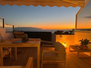 eine Terrasse mit einem Tisch und Stühlen sowie einem Sonnenuntergang in der Unterkunft Casa Oceanico Los Gigantes in Acantilado de los Gigantes