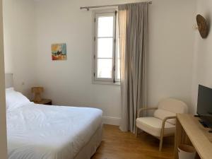 a bedroom with a bed and a chair and a window at La Hugotine in Marseillan