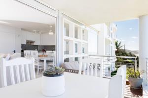 a white dining room with white chairs and a balcony at Ocean Pearl at Chakas Cove - Beachfront Apartment in Ballito
