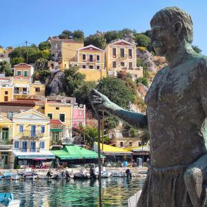 a statue of a woman standing on a boat in a harbor at Lirenou Scala Vista in Symi