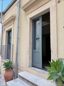 une porte d'un bâtiment avec deux plantes en pot dans l'établissement CoDe24, à Noto
