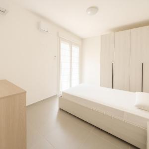 a white bedroom with a large bed and a window at Modern apartment with parking in Lignano Sabbiadoro