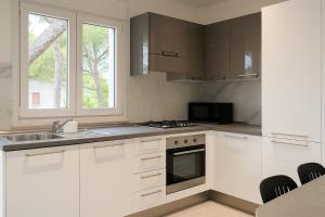 Una cocina con gabinetes blancos y un fregadero y una ventana. en Garden apartment with parking, en Lignano Sabbiadoro 1 foto más