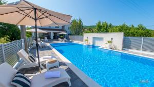 a swimming pool with chairs and an umbrella at Villa Dar Počitelj in Čapljina