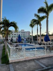 a pool with palm trees and tables and blue umbrellas at Apartamento completo condomínio Ônix in Campos dos Goytacazes