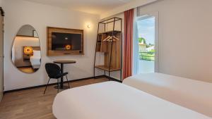 a bedroom with a bed and a table and a mirror at KYRIAD DAX - Saint Paul lès Dax in Saint-Paul-lès-Dax