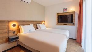 a hotel room with two beds and a tv at KYRIAD DAX - Saint Paul lès Dax in Saint-Paul-lès-Dax