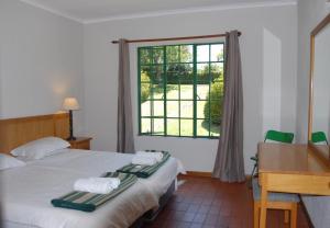 a bedroom with a bed and a desk and a window at Kloofsig Holiday Cottages in Graskop