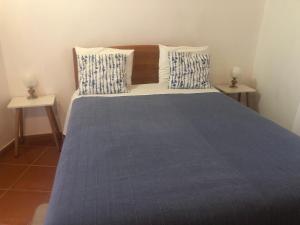 a bedroom with a bed with a blue blanket and two tables at Sudoeste Guest House in Odeceixe