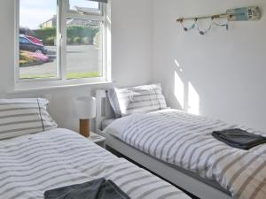 two beds in a white room with a window at Eider Cottage in Embleton