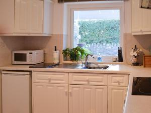 a kitchen with white cabinets and a sink and a window at Fairways in Beadnell