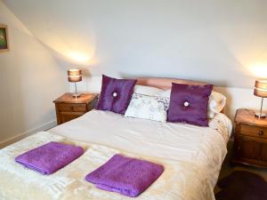 Bydand Cottage في Melness: سرير مع وسائد أرجوانية ومناشف أرجوانية عليه