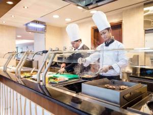 two chefs preparing food in a restaurant kitchen at Grand Mercure Majlis Residences in Abu Dhabi