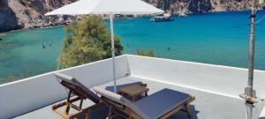 a balcony with chairs and an umbrella and the ocean at Salty Kisses and Sandy Toes in Firopótamos