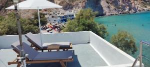 a balcony with chairs and an umbrella and a beach at Salty Kisses and Sandy Toes in Firopótamos
