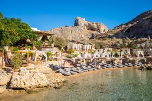 a beach with chaise lounges and chairs and a mountain at Villa Athina in Kalathos