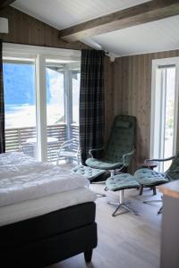 a bedroom with a bed and a chair and windows at Grande Hytteutleige og Camping in Geiranger