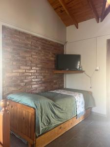 une chambre avec un lit avec une télévision sur un mur de briques dans l'établissement cabañas Samay-Piskho, à Santa Rosa de Calamuchita