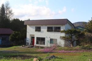 a white house with a red door in a field at 宿　大都会 in Nishitappu