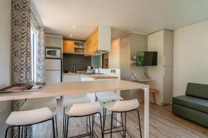 a kitchen with a table and some white stools at Cocon Marin dans Camping 5 étoiles in Vendres-Plage